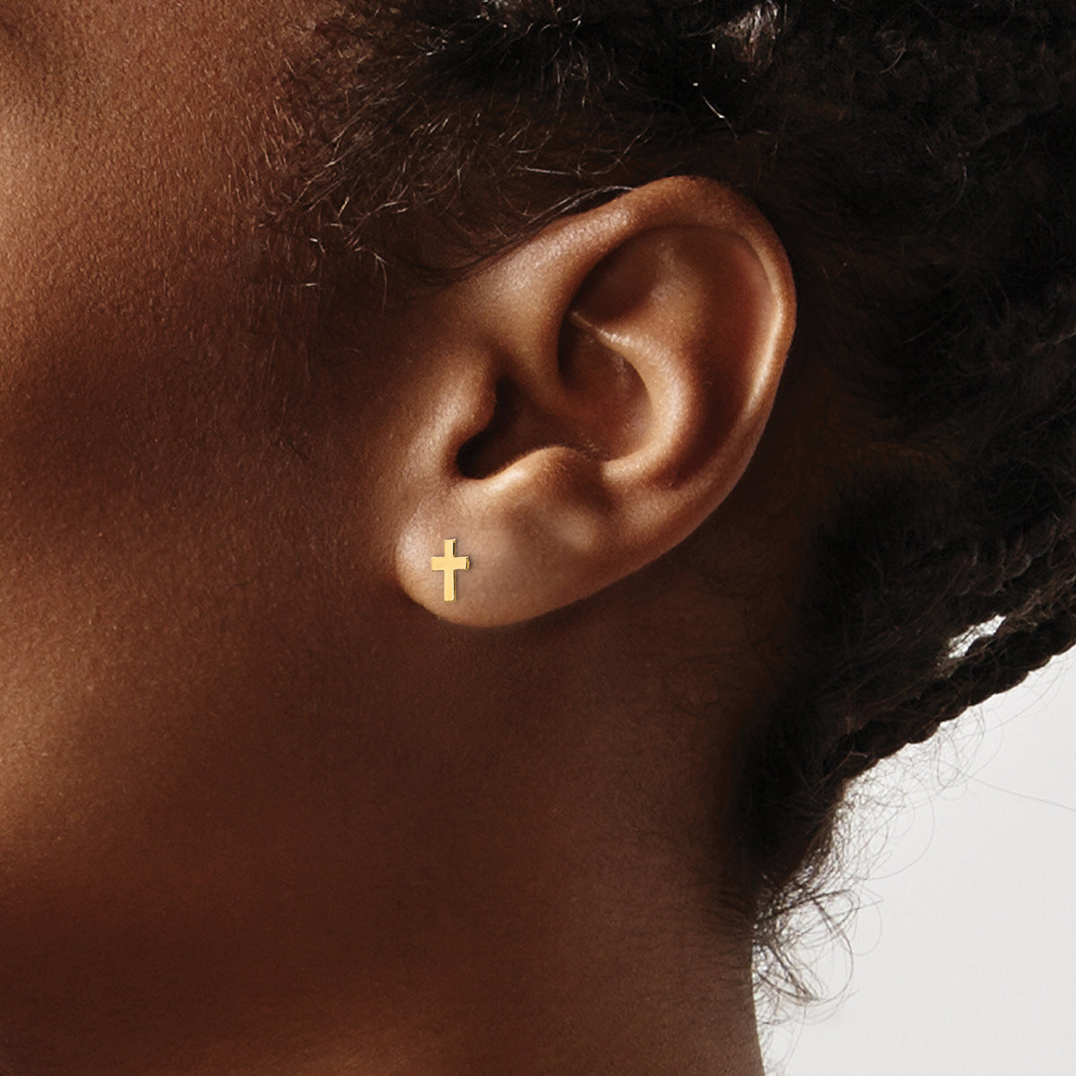 Children’s 14K yellow gold tiny cross earrings shown on ear