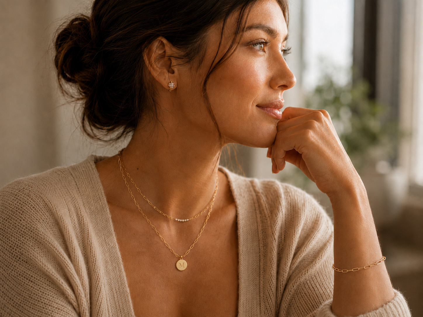 Woman wearing layered gold paperclip jewelry and an initial disc pendant