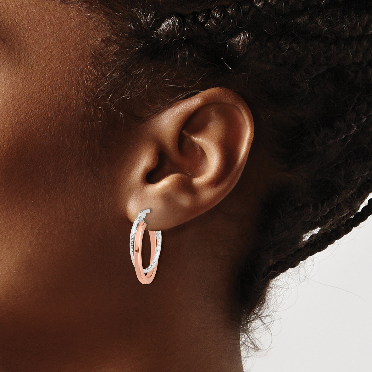 Rose-tone twisted oval hoop earrings worn on ear